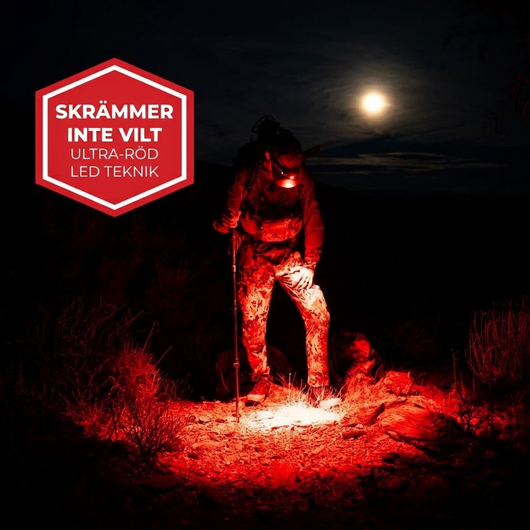 Jägare i terräng på natten med pannlampans röda ULTRA RED-läge tänt under fullmåne